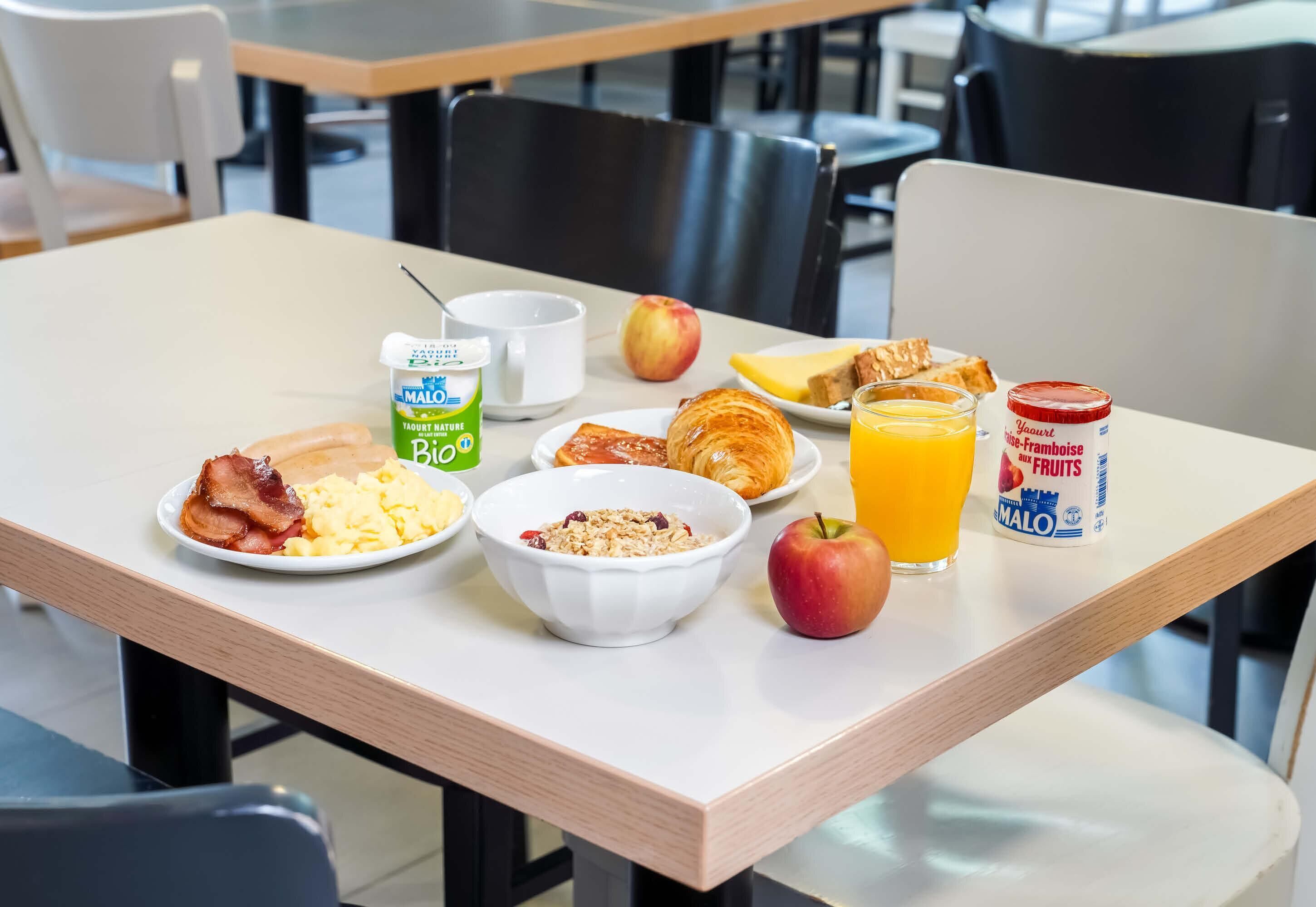 A breakfast table with plates of food, a bowl of cereal, a glass of orange juice, and a jar of jam.
