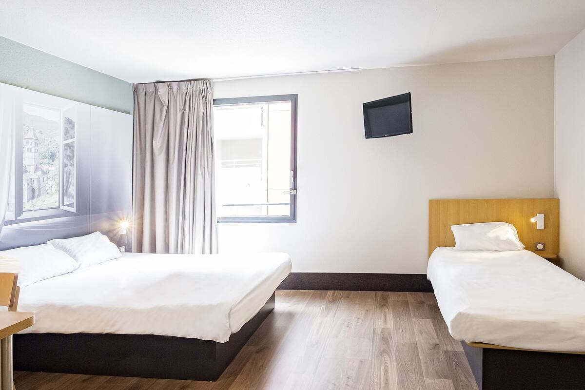 Una habitación de hotel con dos camas, un televisor montado en la pared y una ventana con cortinas.