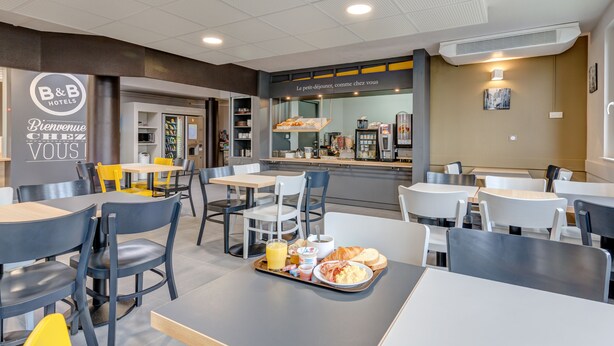 A B&B hotel's breakfast area with tables, chairs, and a tray with breakfast items. - B&B HOTEL Goussainville CDG (Goussainville)