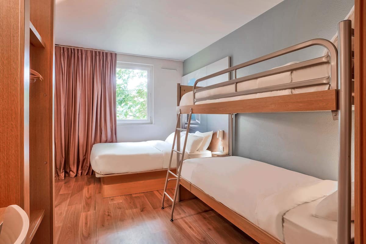 Una habitación con dos literas, un armario de madera, una ventana con cortinas y piso de madera.