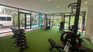 Un gimnasio con suelo verde, equipo de levantamiento de pesas y amplios ventanales que ofrecen vistas al exterior.