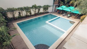 Una piscina rectangular con borde de azulejos, rodeada de plantas en macetas y mobiliario de exterior.
