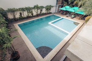 Una piscina rectangular con borde de azulejos, rodeada de plantas en macetas y mobiliario de exterior.