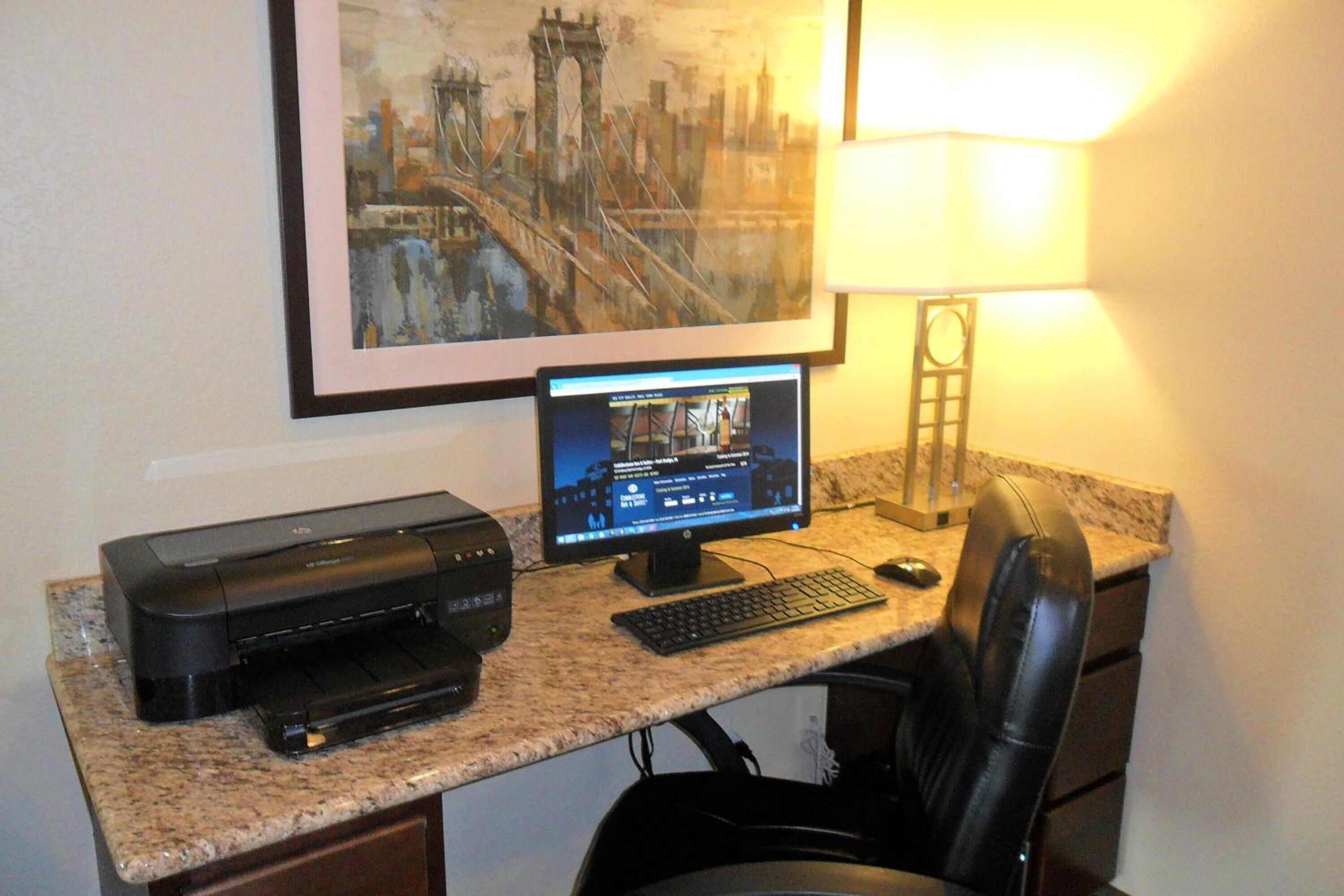 A home office setup with a desktop computer, printer, and a framed cityscape painting on the wall.