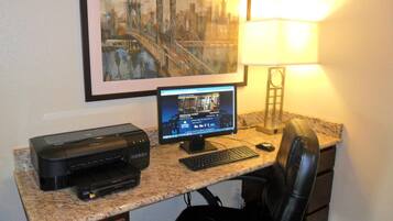 A home office setup with a desktop computer, printer, and a framed cityscape painting on the wall.