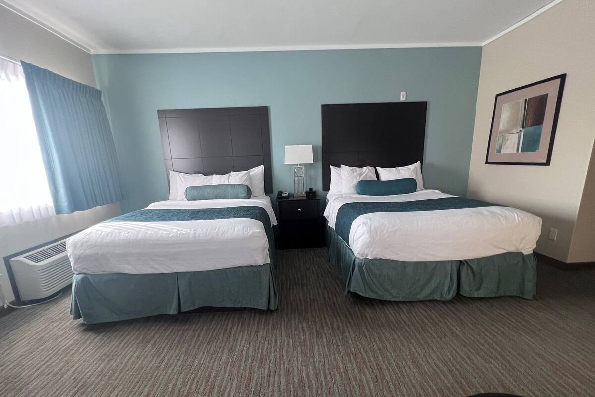 A hotel room with two beds, a nightstand, a lamp, and a framed picture on the wall.
