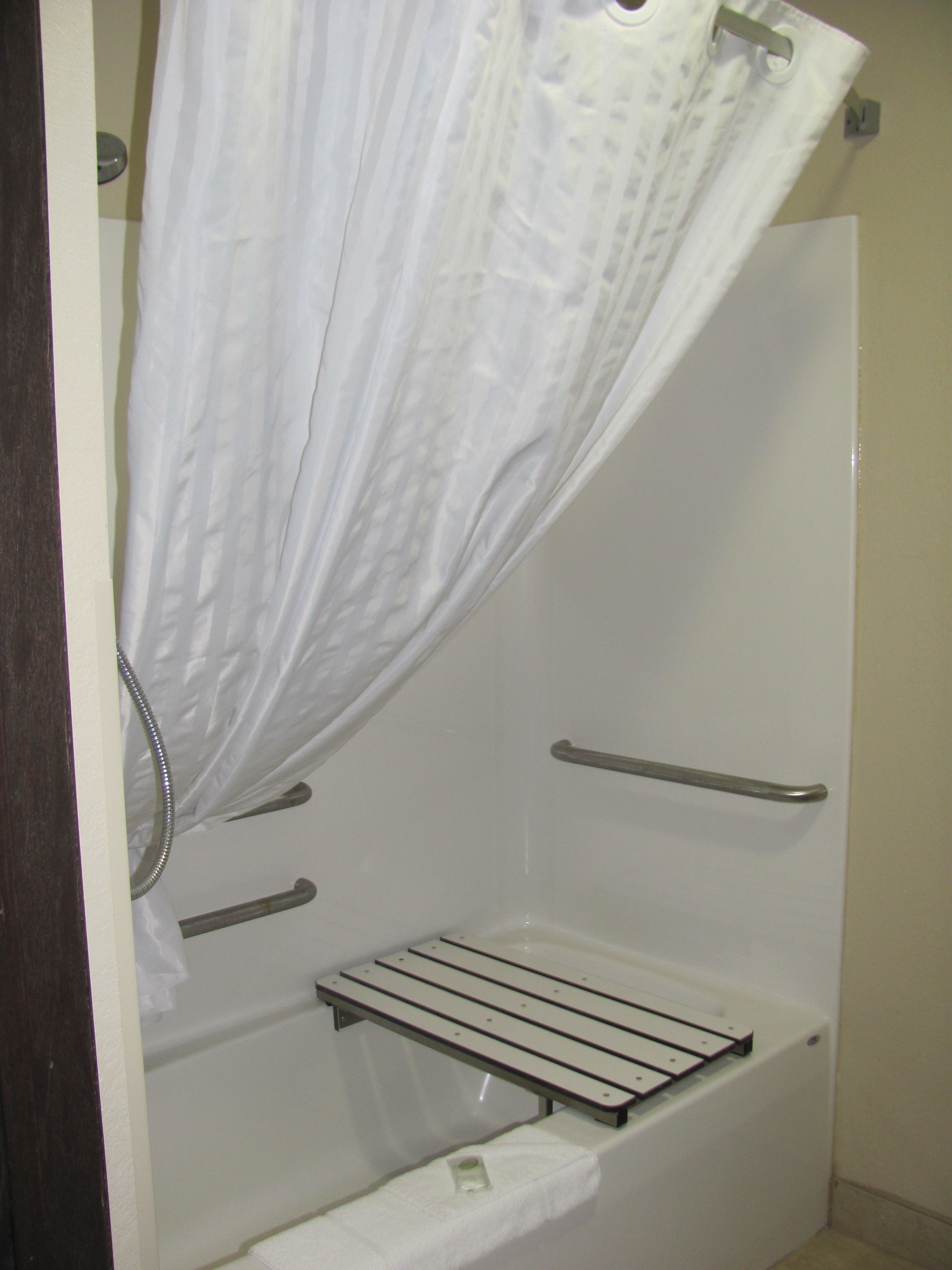 A shower with a white curtain, a handheld showerhead, a towel rack, and a shelf.