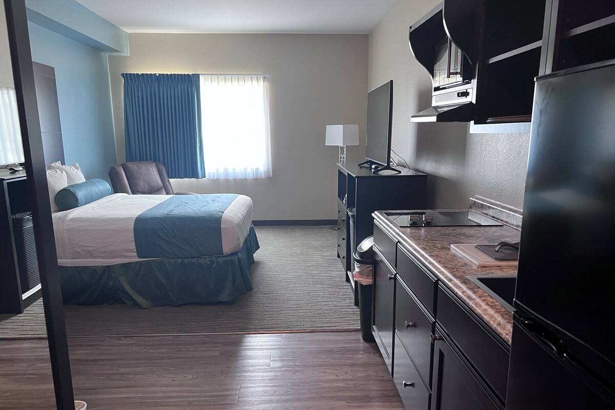 A hotel room with a bed, a desk, a refrigerator, and a window with curtains.