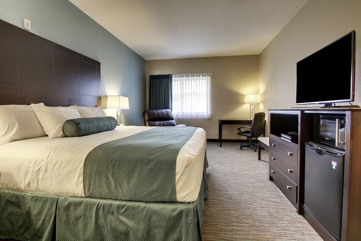 A hotel room with a large bed, a desk with a chair, a television, and a dresser.