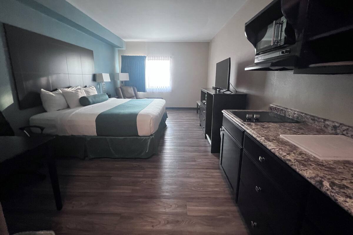 A hotel room with a bed, a desk, a TV, and a kitchenette.