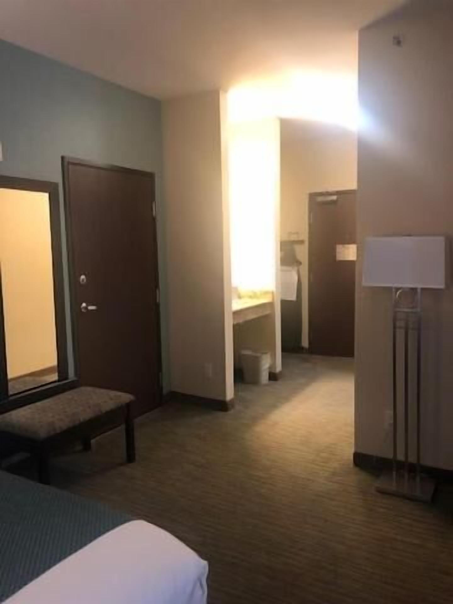 A hotel room with a bed, a desk, a chair, a mirror, a lamp, and a door.