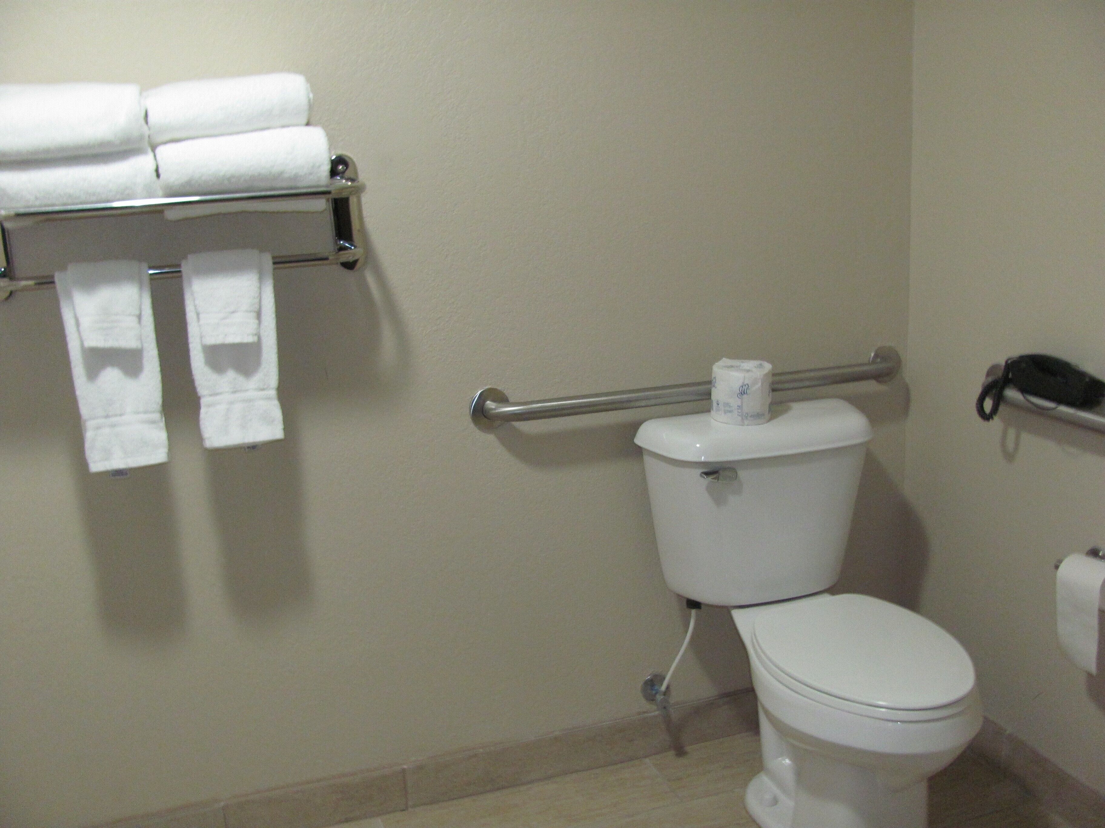 Ein Badezimmer mit Toilette, Handtuchhalter mit gefalteten Handtüchern und Toilettenpapierhalter.