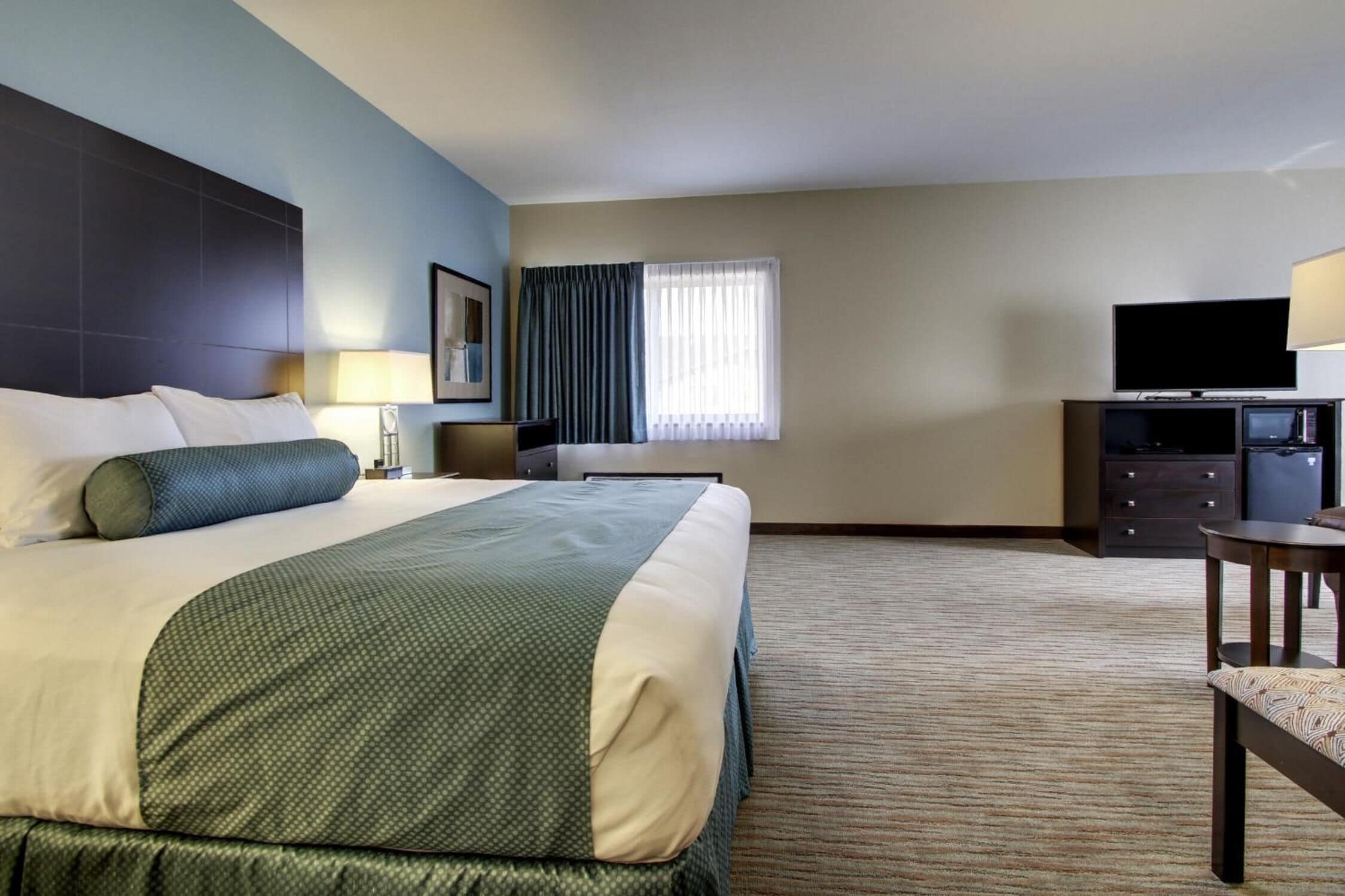 A hotel room with a large bed, a desk, a television, and a window with curtains.
