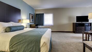 A hotel room with a large bed, a desk, a television, and a window with curtains.