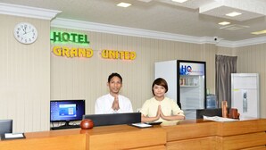 Un comptoir de réception d’hôtel avec une horloge, un ordinateur et une enseigne sur laquelle on peut lire : « HÔTEL GRAND UNITED ».