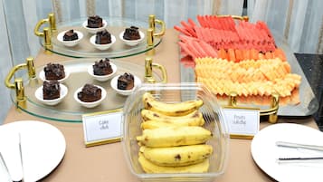 A buffet table with various food items including cakes, bananas, and fruits.