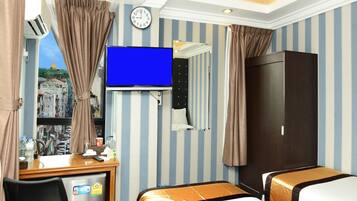 A hotel room with two beds, a TV, a desk with a fridge, a clock, and a view of a cityscape.