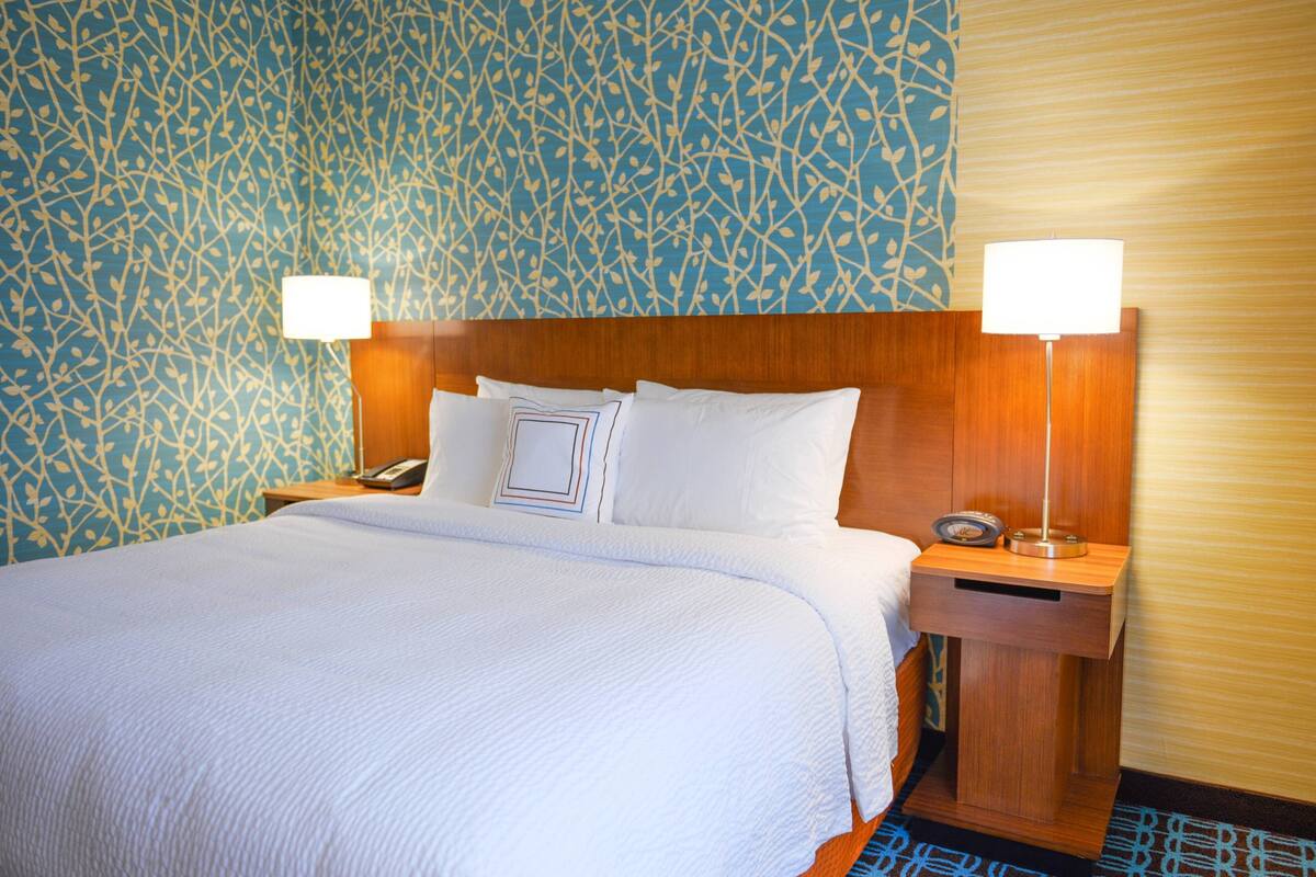 Ein Hotelzimmer mit einem großen Bett, zwei Nachttischen mit Lampen, einer Wand mit Muster und einem hölzernen Kopfteil.