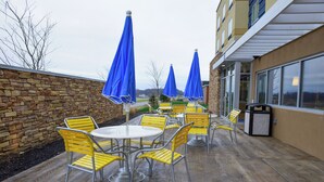 An outdoor patio with yellow chairs and blue umbrellas, a stone wall, and a building with large windows. - Fairfield Inn & Suites Canton South (Canton)