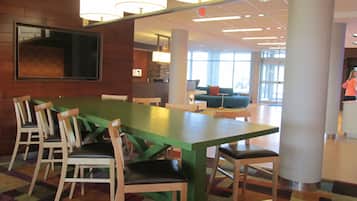 A modern dining area with a green table and wooden chairs, a sofa, and a large window providing natural light.
