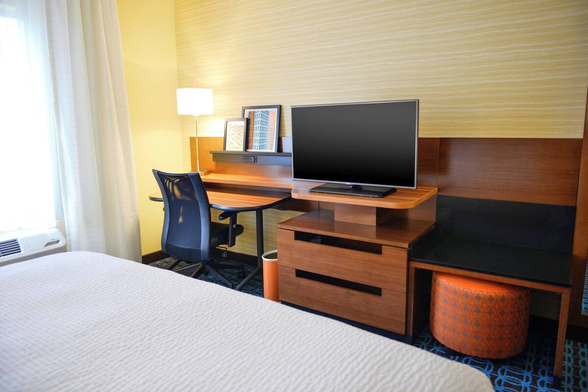 Ein Hotelzimmer mit einem Bett, einem Schreibtisch mit Computer, einem Stuhl, einer Lampe und einem Papierkorb.