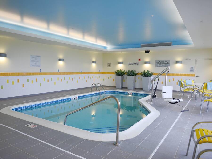 An indoor swimming pool with clear lane markings, a lifeguard chair, and yellow chairs around the pool area.