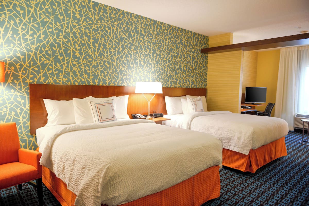 Ein Hotelzimmer mit zwei Betten, einem Schreibtisch, einem Stuhl und einem Fernseher.