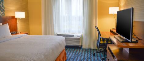 A hotel room with a bed, a desk with a TV, a chair, a desk lamp, and a window with curtains.