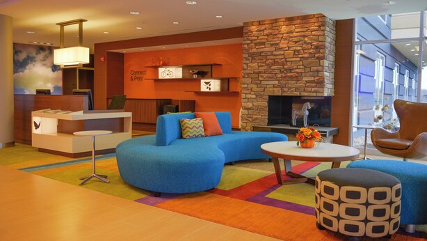 A modern hotel lobby with a blue sofa, a round coffee table, a stone fireplace, and a reception desk. - Fairfield Inn & Suites Canton South (Canton)