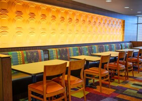 Un restaurante con cabinas y mesas, un muro con diseño y una alfombra colorida.