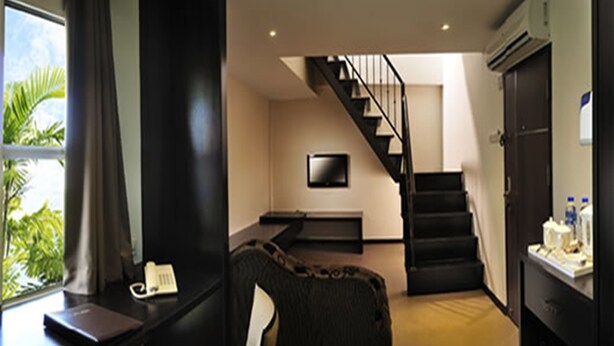 Habitación de hotel moderna con escritorio, una silla, una cama, televisión, una escalera y una ventana con vistas a zonas verdes.