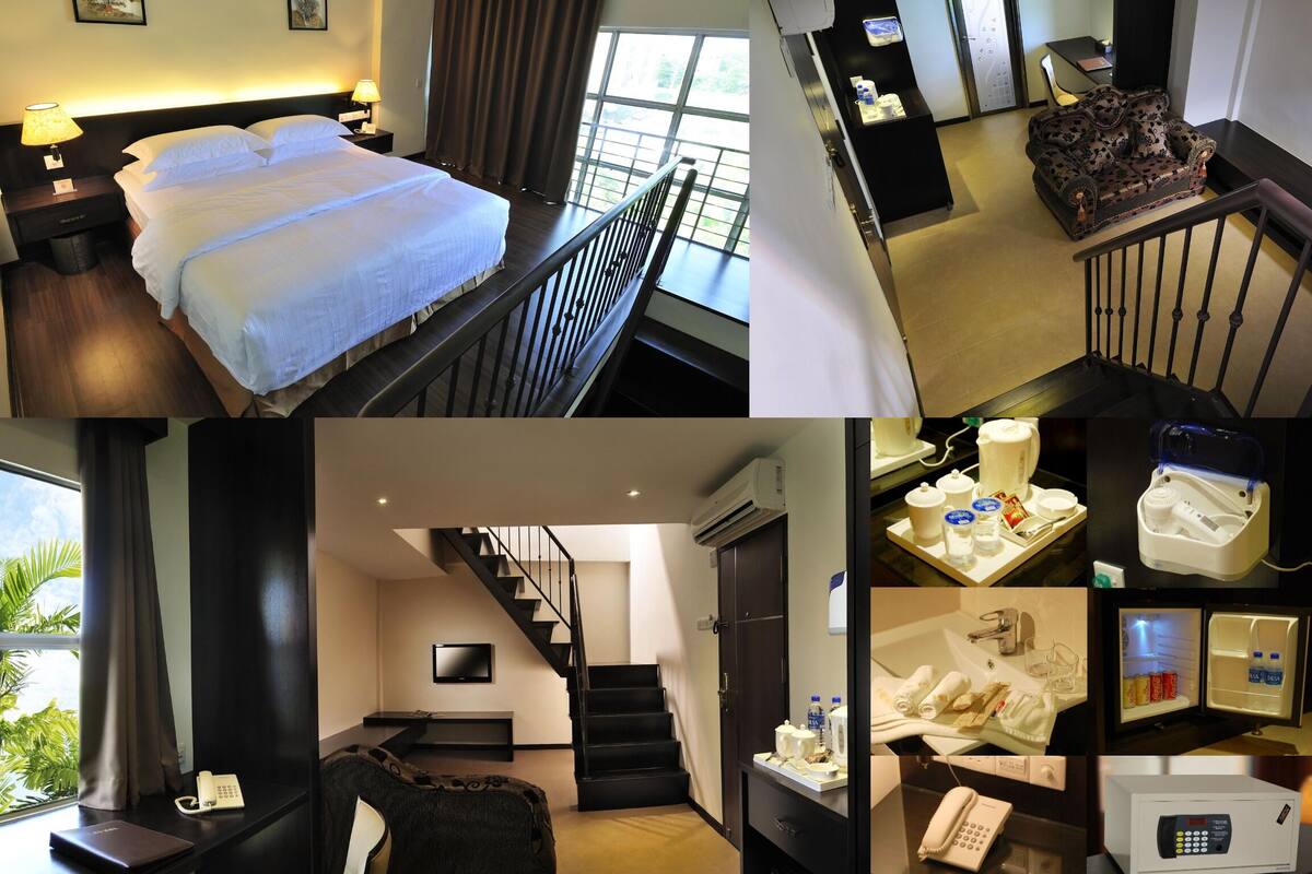 A hotel room with a bed, a desk with a lamp, a chair, a TV, a staircase, and a bathroom with a shower, toilet, and sink.