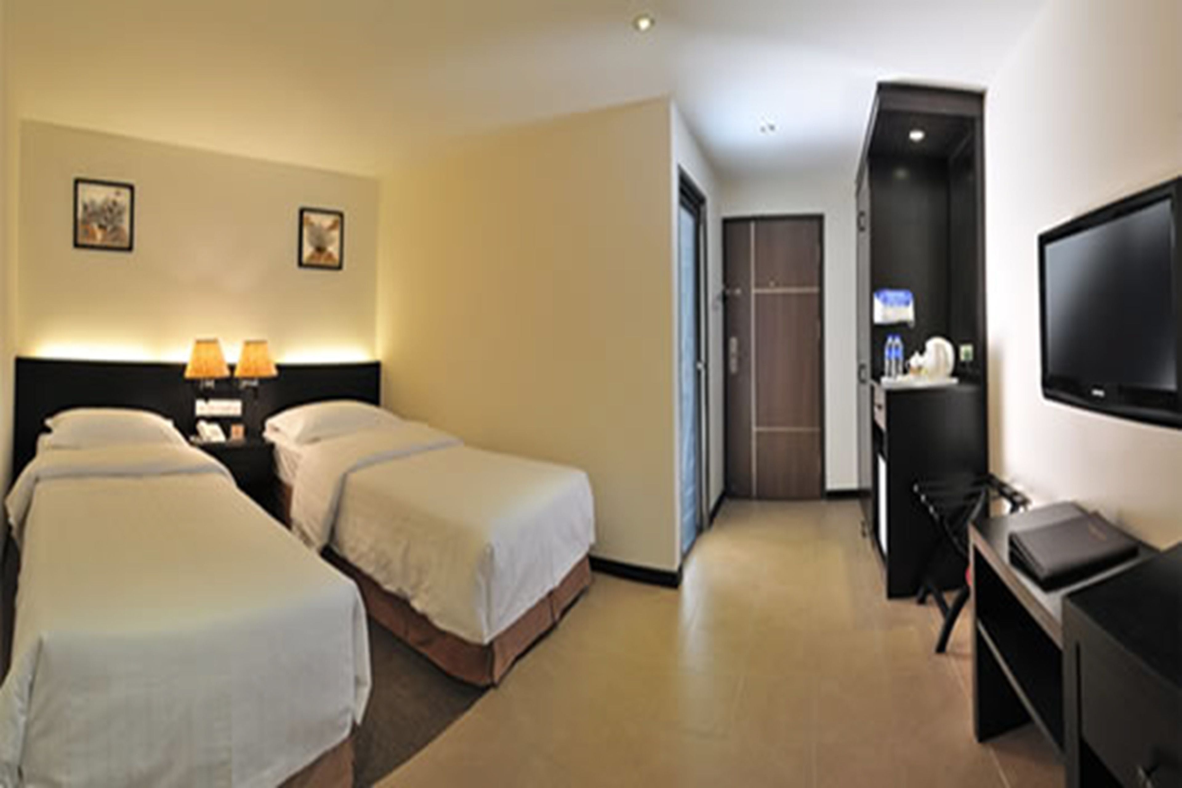 Ein Hotelzimmer mit zwei Betten, einem Schreibtisch mit Computer, einem Fernseher und einer Minibar.
