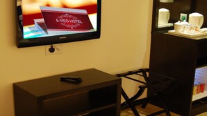 Un televisor mostrando un anuncio de E-RED HOTEL, un control remoto sobre una mesa de madera y un minibár con café y té.