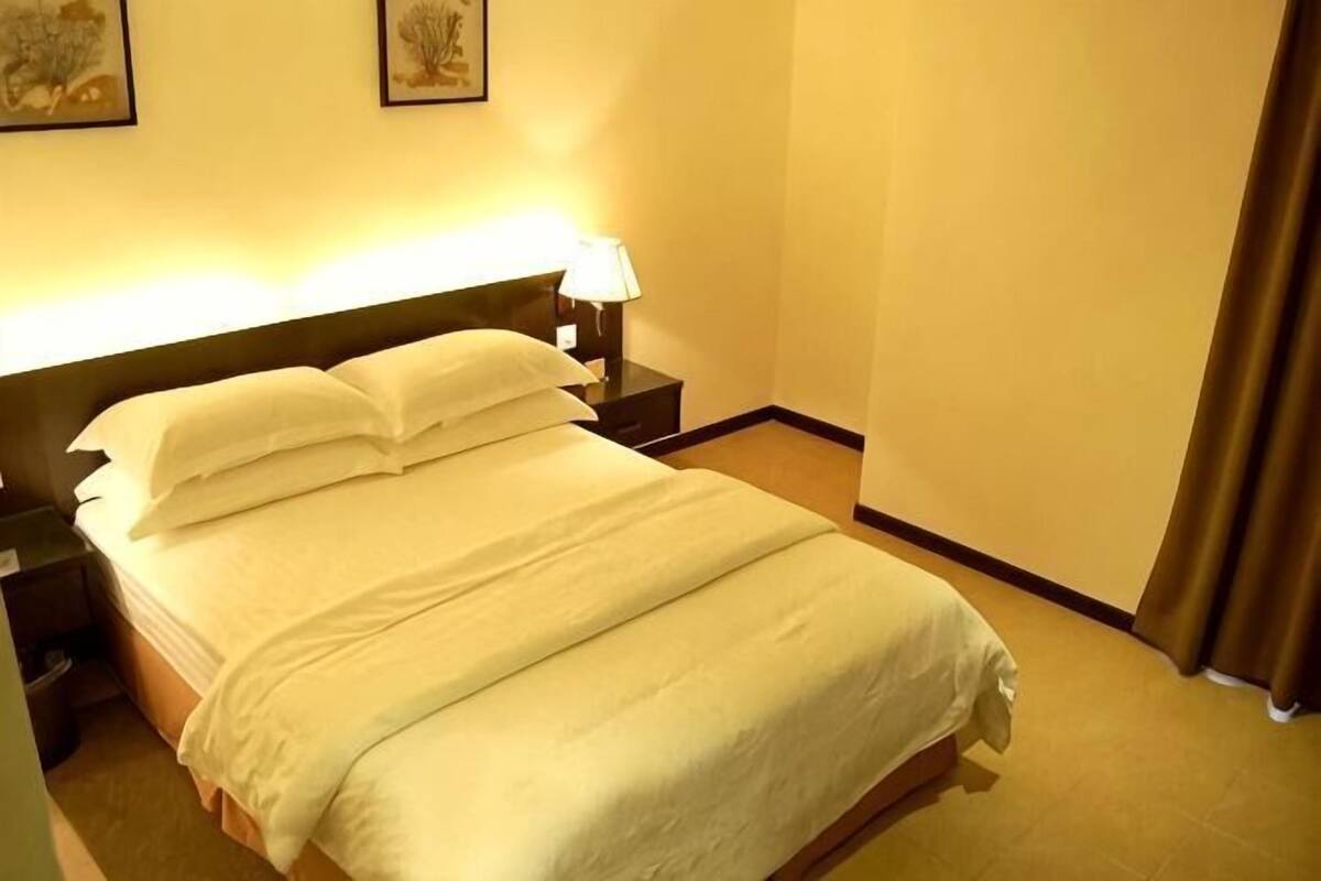A neatly made bed with pillows and a blanket, a bedside lamp, and a nightstand.