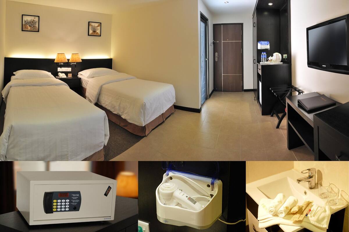 A hotel room with two beds, a desk with a laptop, a TV, a minibar, and a bathroom with a shower, toilet, and sink.