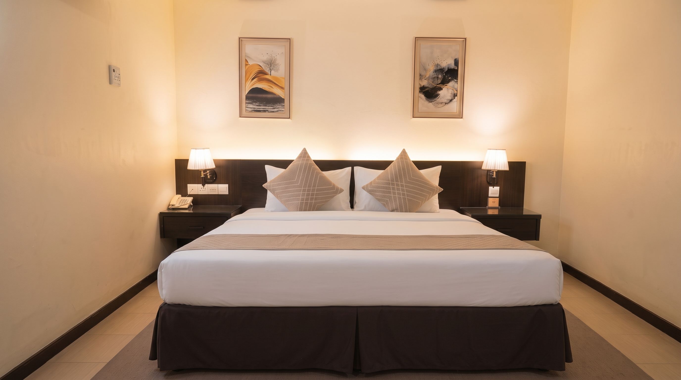 A hotel room with a large bed, two bedside tables with lamps, and two framed artworks on the wall.