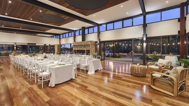 A spacious indoor area with multiple tables set for dining, a stone fireplace, wicker furniture, and large windows offering views of the outdoors. - Eight Willows Retreat (Metricup)