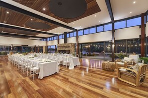 A spacious indoor area with multiple tables set for dining, a stone fireplace, wicker furniture, and large windows offering views of the outdoors. - Eight Willows Retreat (Metricup)