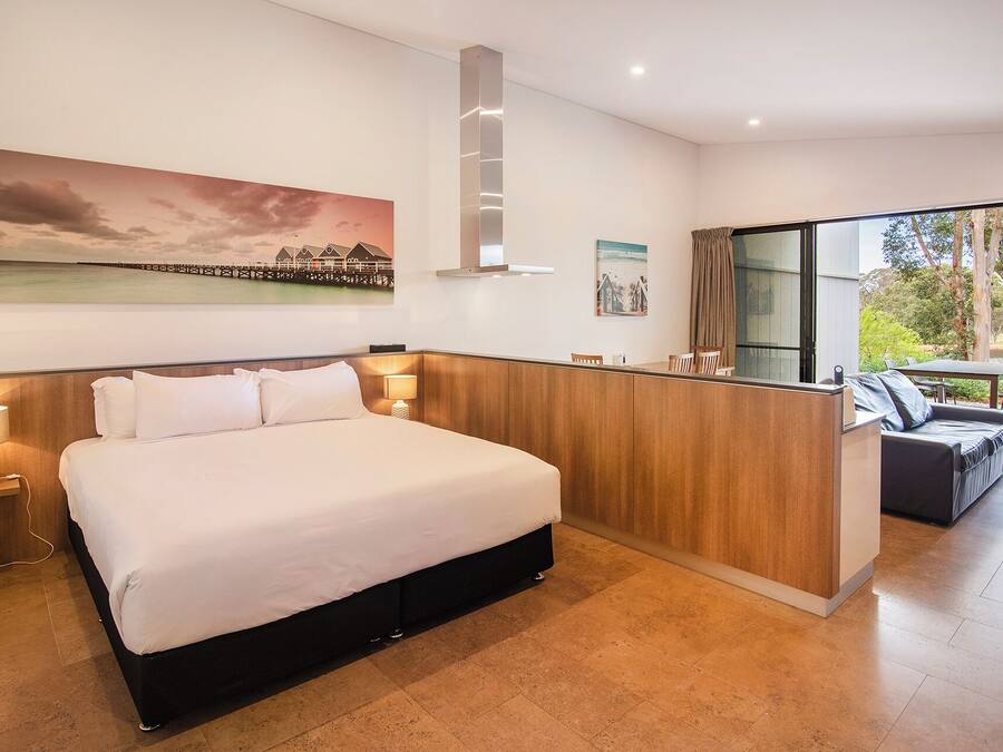 Quarto de hotel moderno com uma cama grande, cabeceira de madeira, uma pequena escrivaninha e vista para o exterior através de uma grande janela.