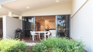 A modern house with a patio area featuring a table and chairs, surrounded by greenery. - Eight Willows Retreat (Metricup)