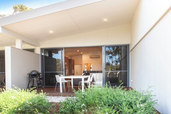 A modern house with a patio area featuring a table and chairs, surrounded by greenery. - Eight Willows Retreat (Metricup)