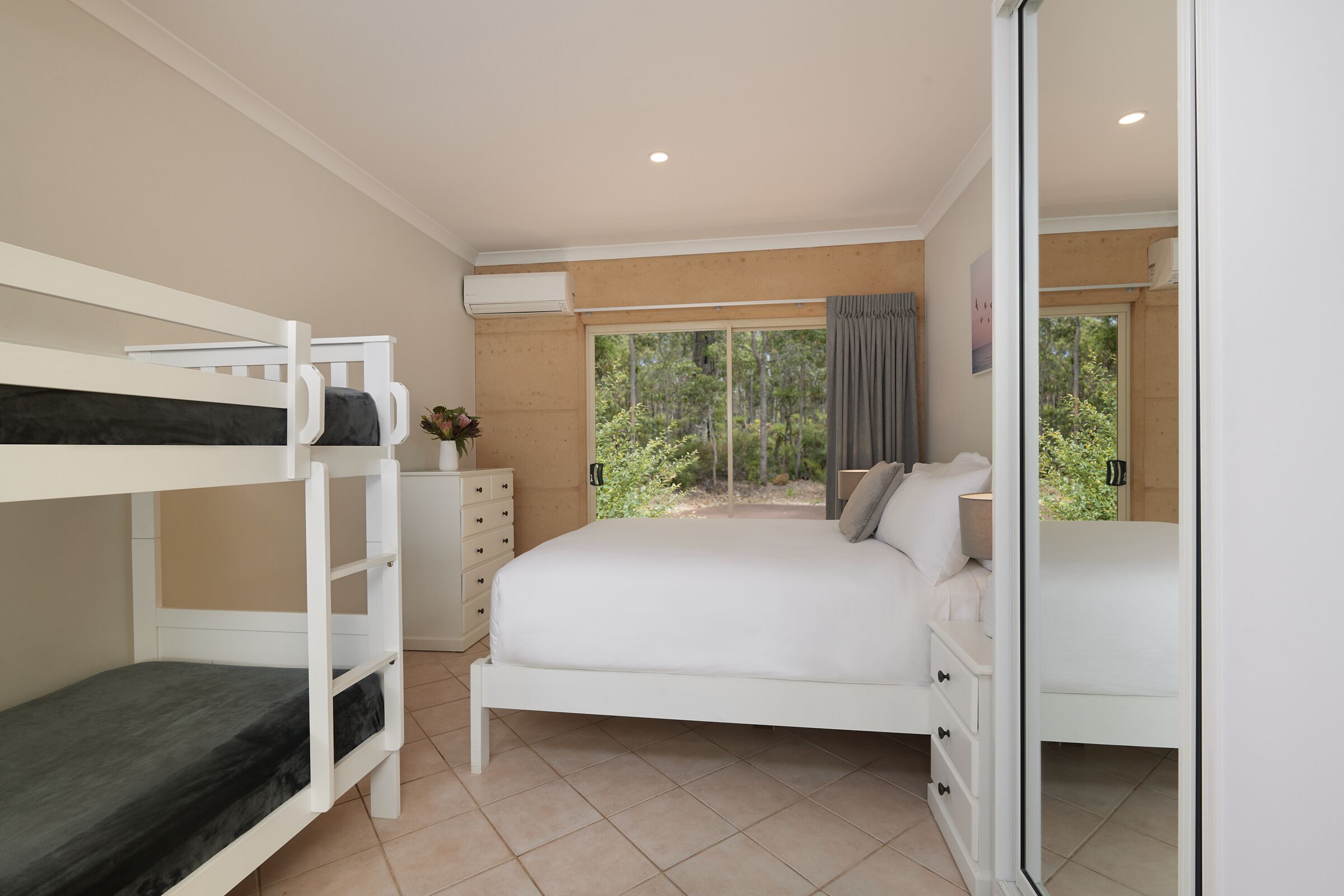 Un dormitorio con literas, una cama grande, un aparador y vistas al verdor exterior.