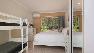 Un dormitorio con literas, una cama grande, un aparador y vistas al verdor exterior.