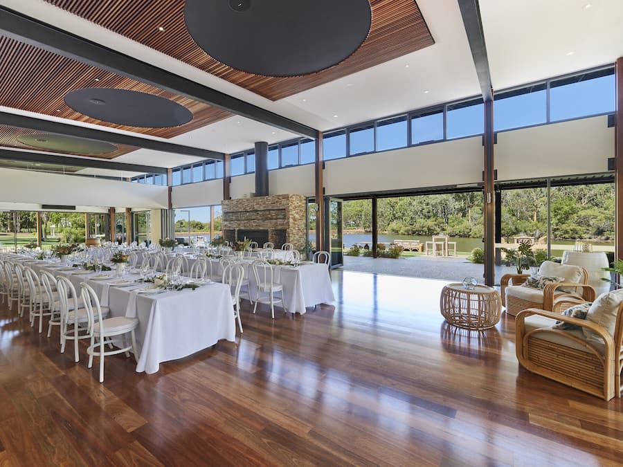 Un comedor interior amplio con largas mesas dispuestas para una comida, grandes ventanales que ofrecen vistas al exterior y un diseño de techo moderno.
