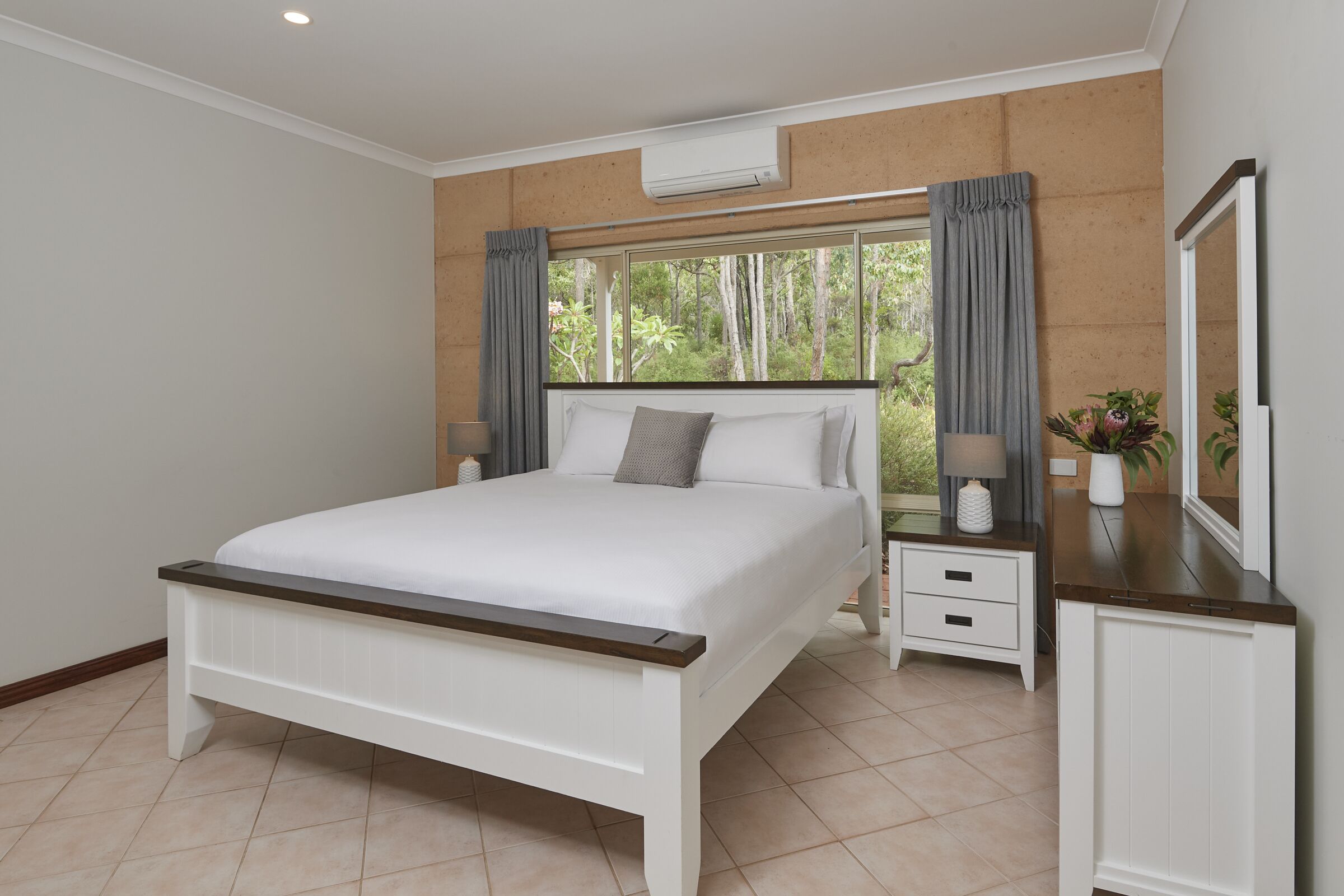 A bedroom with a bed, nightstands, a dresser, and a large window with curtains.