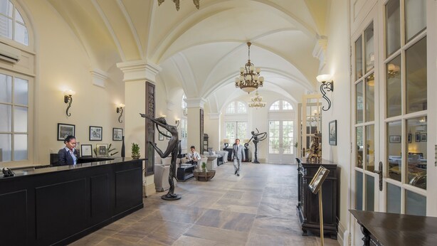 A spacious lobby with high ceilings, a reception desk, and a chandelier. - Palace Gate Hotel & Residence by EHM (Phnom Penh)