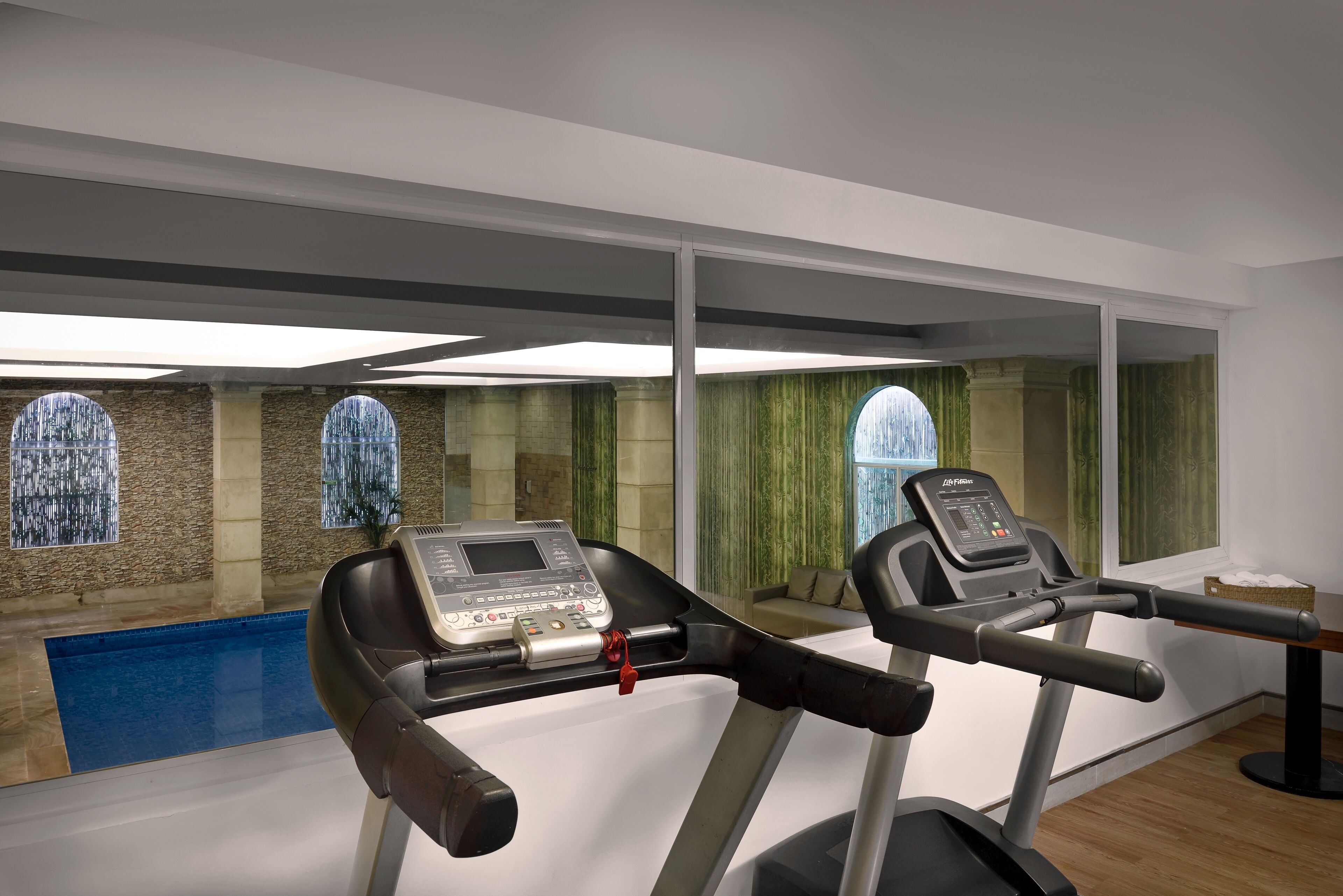 Un gimnasio con cintas de correr y una piscina, paredes de piedra y ventanas amplias.