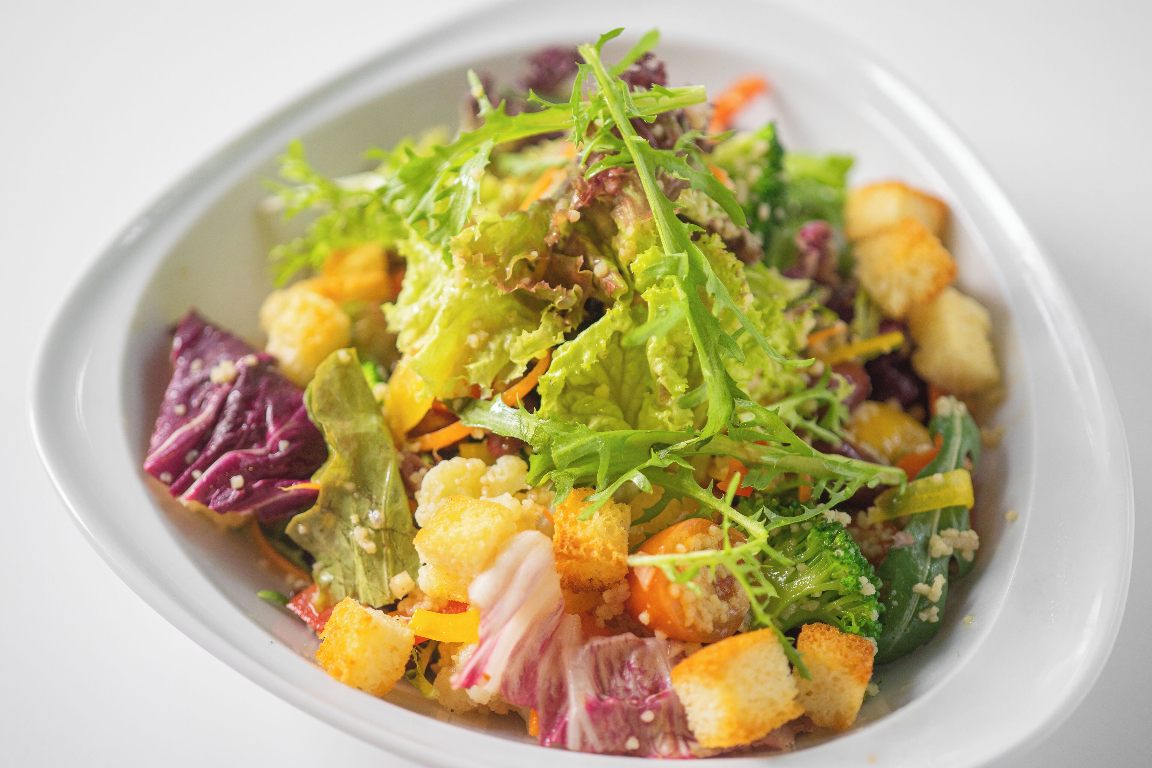 A bowl of salad with various greens, vegetables, and croutons.