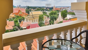 A balcony with a glass table and chairs, overlooking a cityscape with traditional buildings and a temple. - Palace Gate Hotel & Residence by EHM (Phnom Penh)